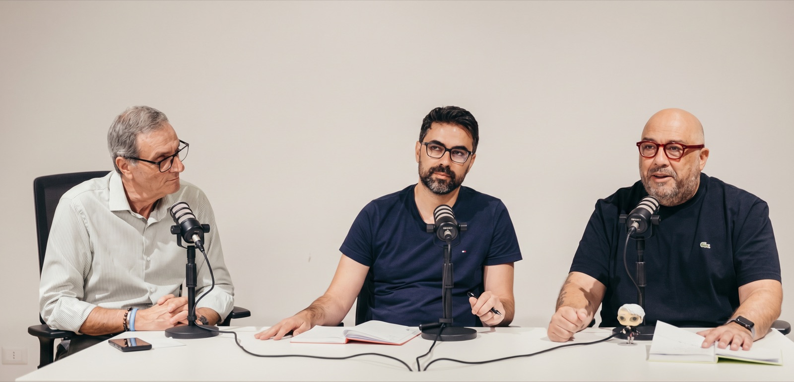 Tre conduttori al tavolo con i microfoni durante una puntata del podcast